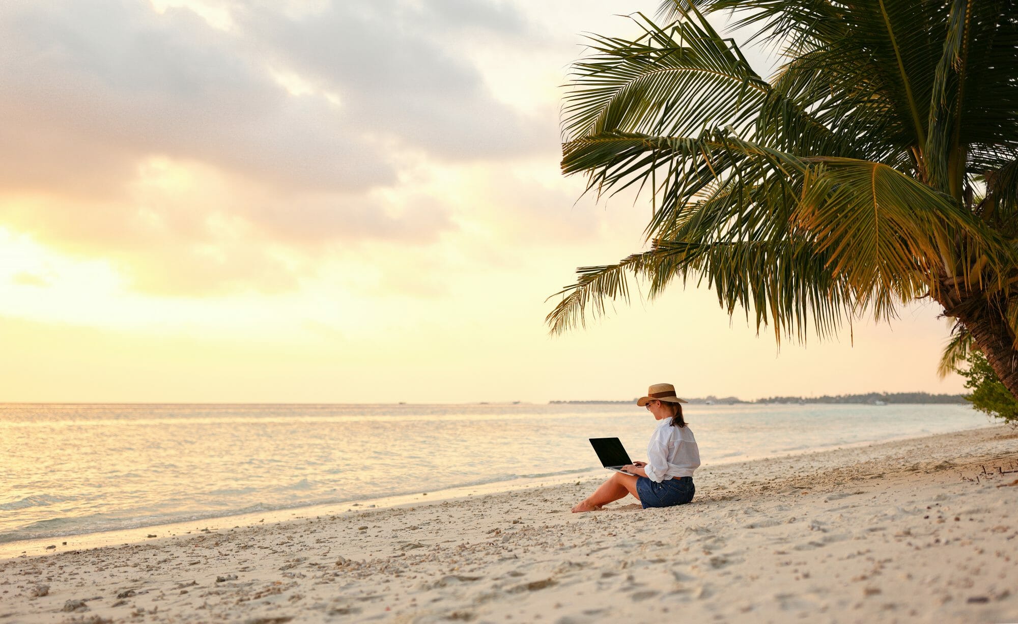 Frau sitzt mit Laptop am Strand